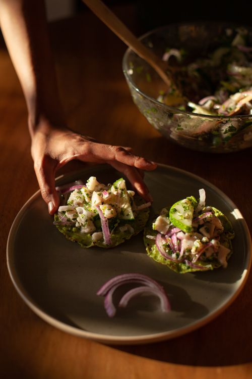 Free Close-up of homemade tostadas with fresh vegetables and a hand plating them on a table. Stock Photo