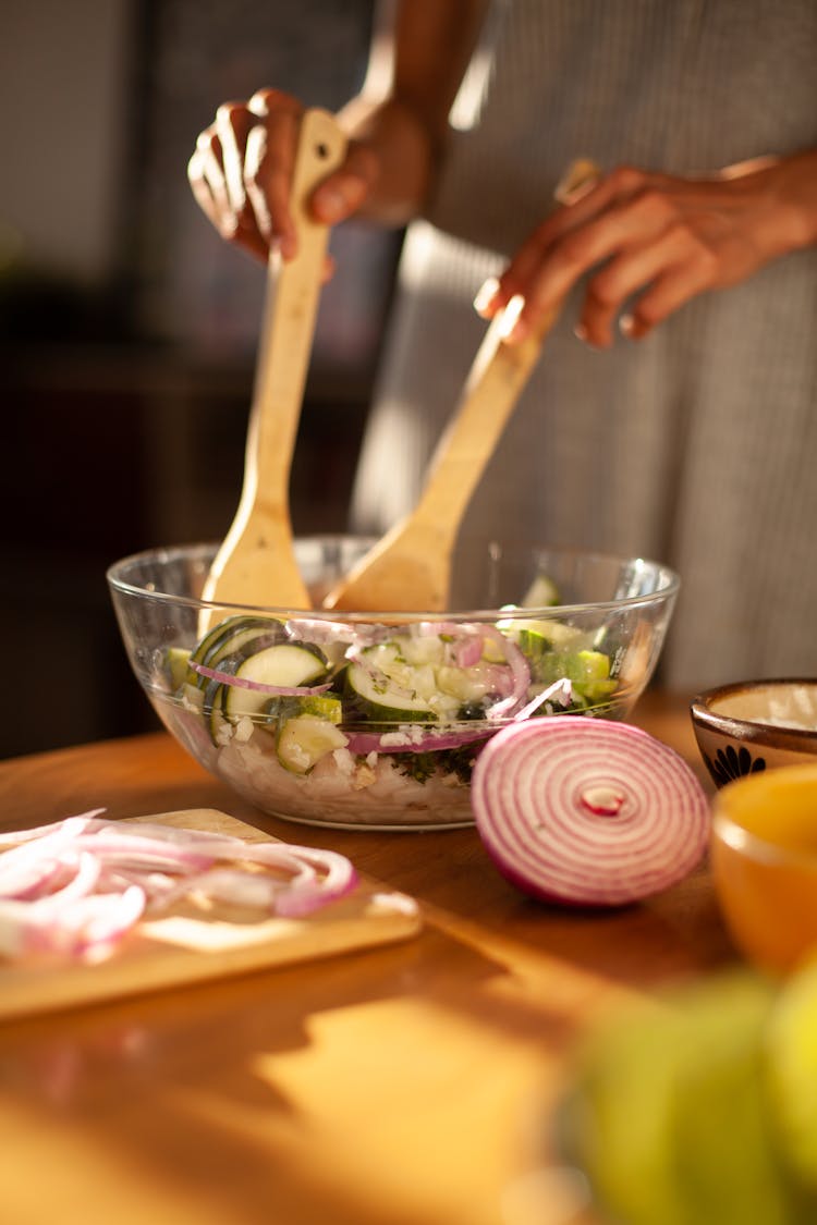 A Person Mixing A Salad On A Glass Bowl