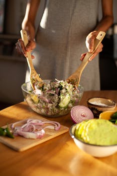 Woman mixing a fresh vegetable salad in a kitchen setting with natural light.