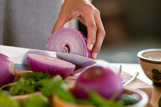 A close-up shot of a hand slicing a red onion on a wooden cutting board, showcasing freshness.