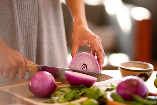 Hands slicing a red onion on a cutting board, showcasing fresh ingredients.