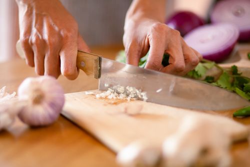 Free Hands chopping fresh garlic and onions on a wooden board in a kitchen setting. Stock Photo