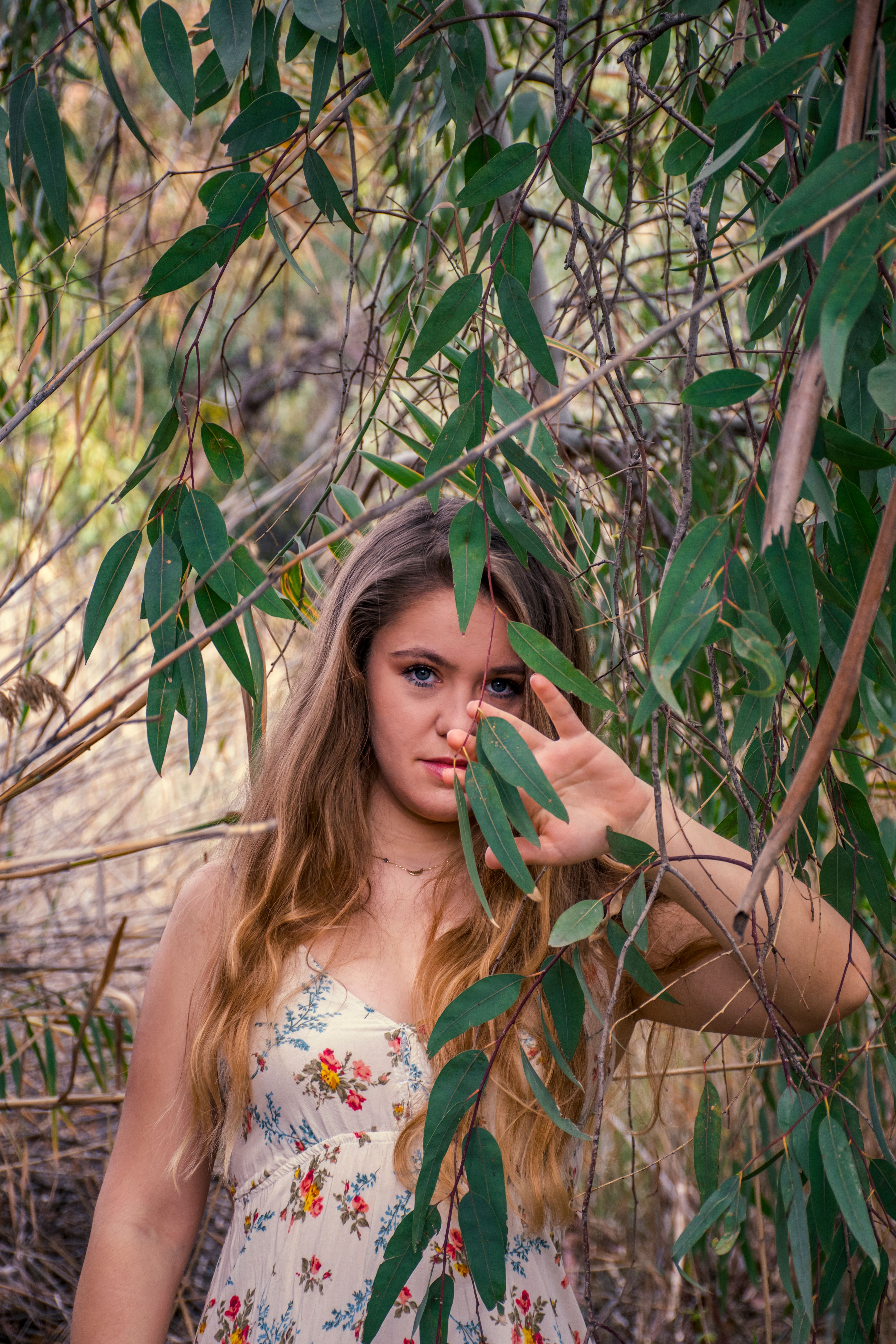 Woman in White Floral Dress Standing beside Green Leaves · Free Stock Photo