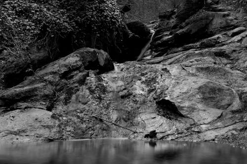 Grayscale Photo of a Body of Water Near Rocks