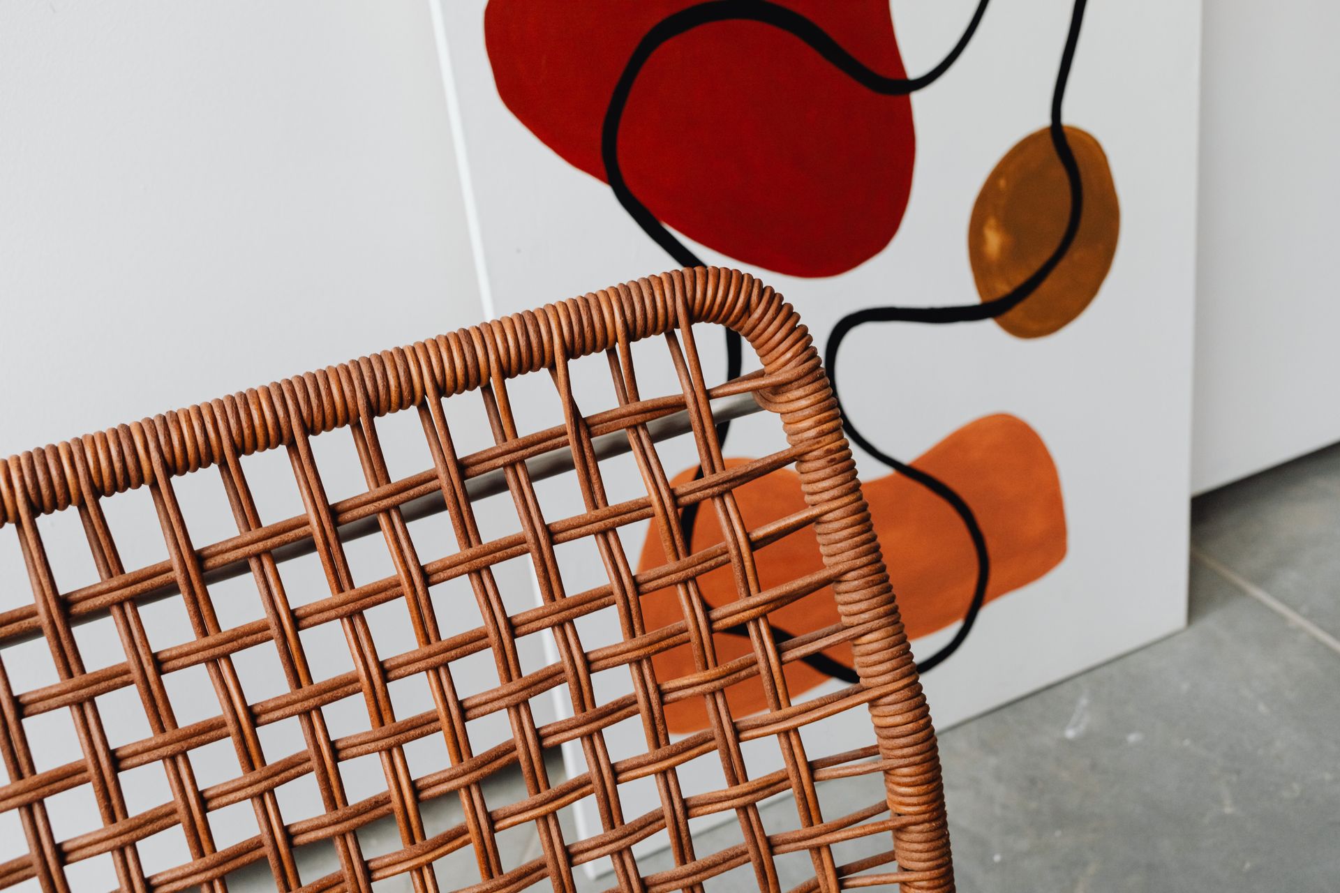 Abstract painting and wicker chair showcasing modern interior design elements.