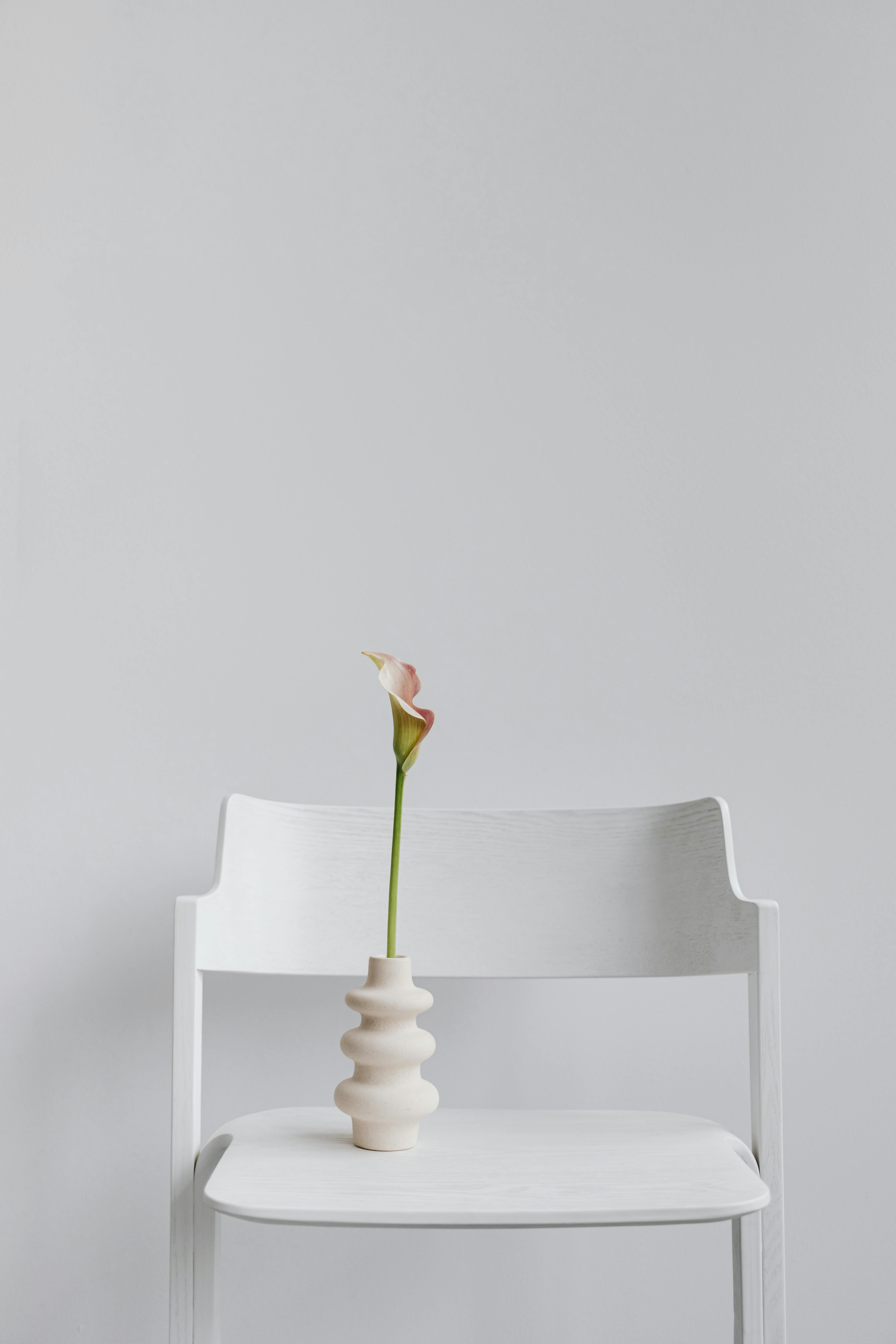 Elegant calla lily in a modern vase on a white chair, showcasing minimalist design on a neutral background.