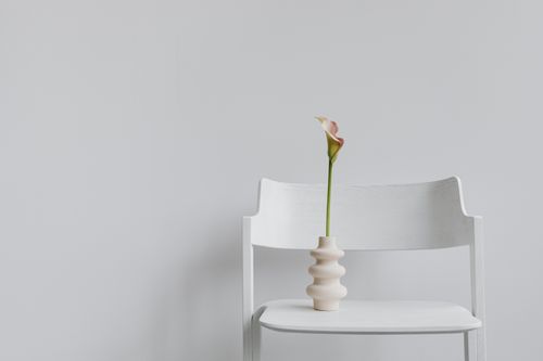 Free A single calla lily in a decorative vase atop a white chair, showcasing minimalist elegance. Stock Photo