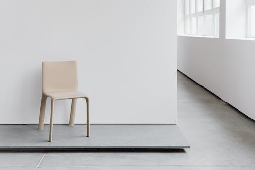 A minimalist beige chair placed in a modern, light-filled room with clean lines.