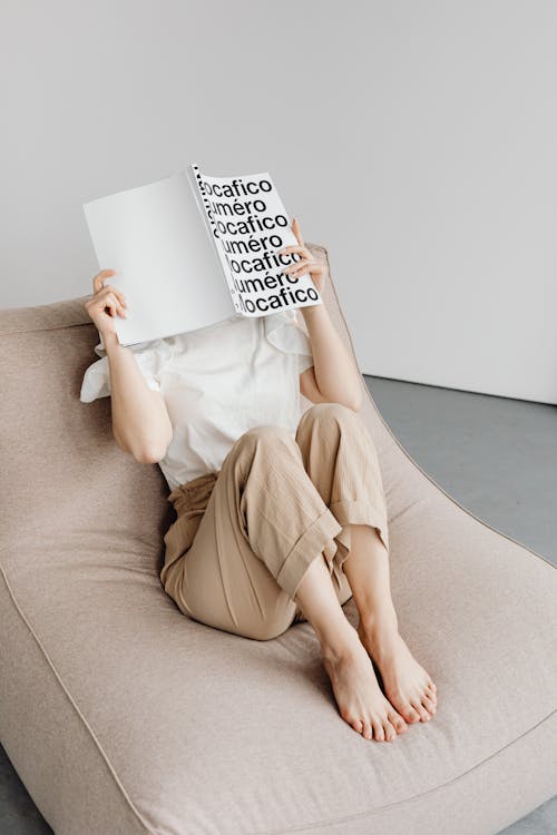 Free A Person Reading a Book while Sitting on a Comfortable Chair Stock Photo