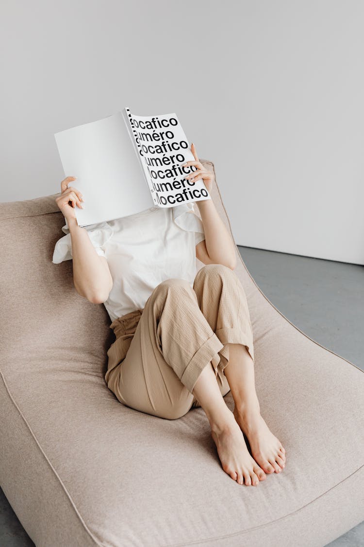 A Person Reading A Book While Sitting On A Comfortable Chair