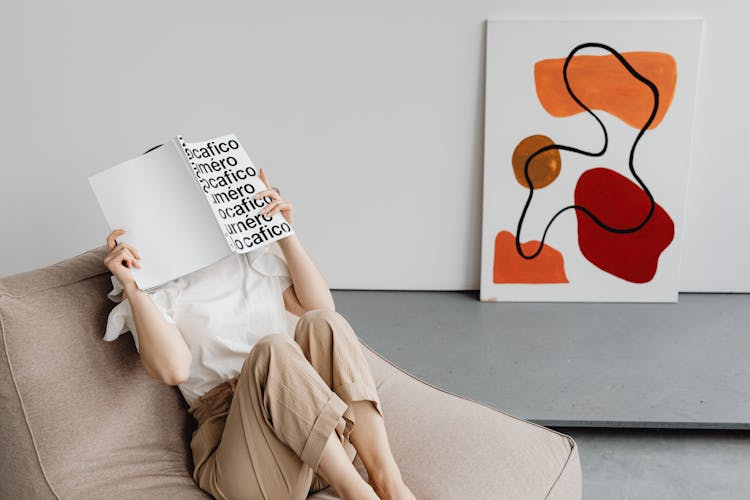 A Person Reading A Book While Sitting On A Comfortable Chair