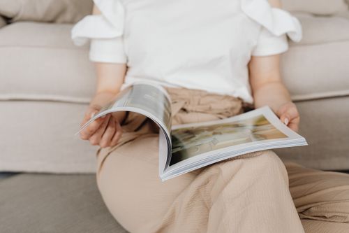 Free A woman in casual attire relaxes indoors while flipping through a magazine. Stock Photo