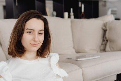 Portrait of a smiling woman seated on a sofa in a modern living room, exuding comfort and warmth — photo by Kaboompics on Pexels