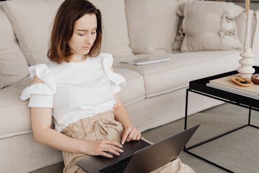 A woman sits on the floor using a laptop for remote work in a stylish, comfortable living room.