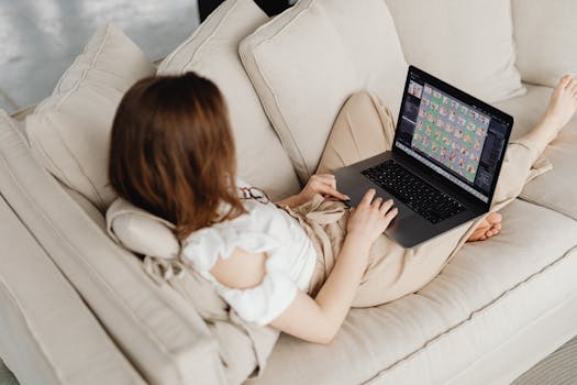 Woman lounging on a sofa, working remotely with a laptop. Casual home office setup.