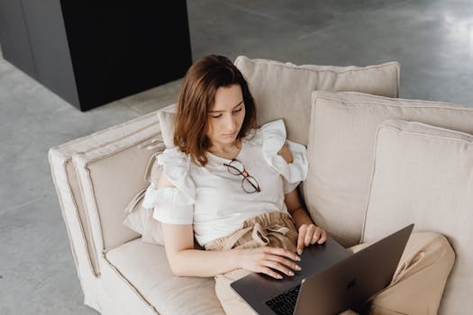 A woman working remotely with a laptop while relaxing on a comfortable sofa indoors.