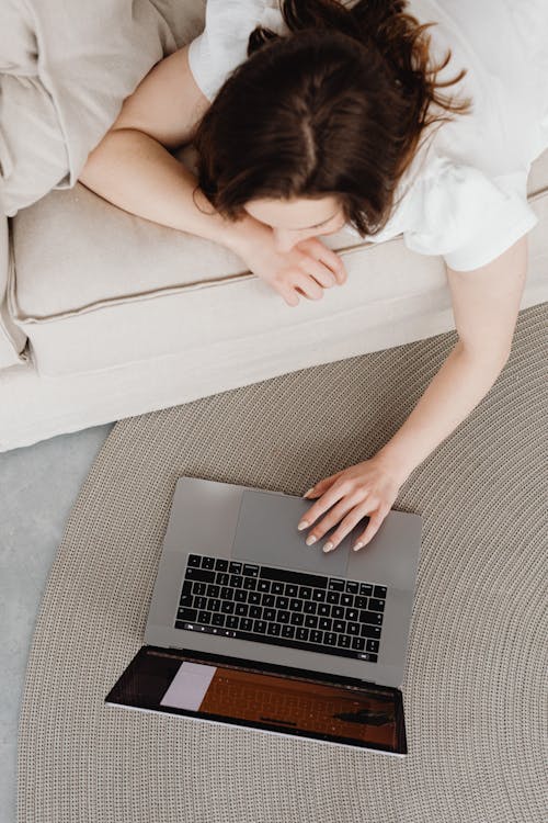 Woman in White Shirt Lying on Sofa while using Laptop