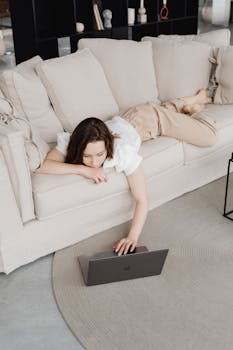 Woman lying on a couch working remotely using a laptop, capturing the essence of modern digital nomad lifestyle.
