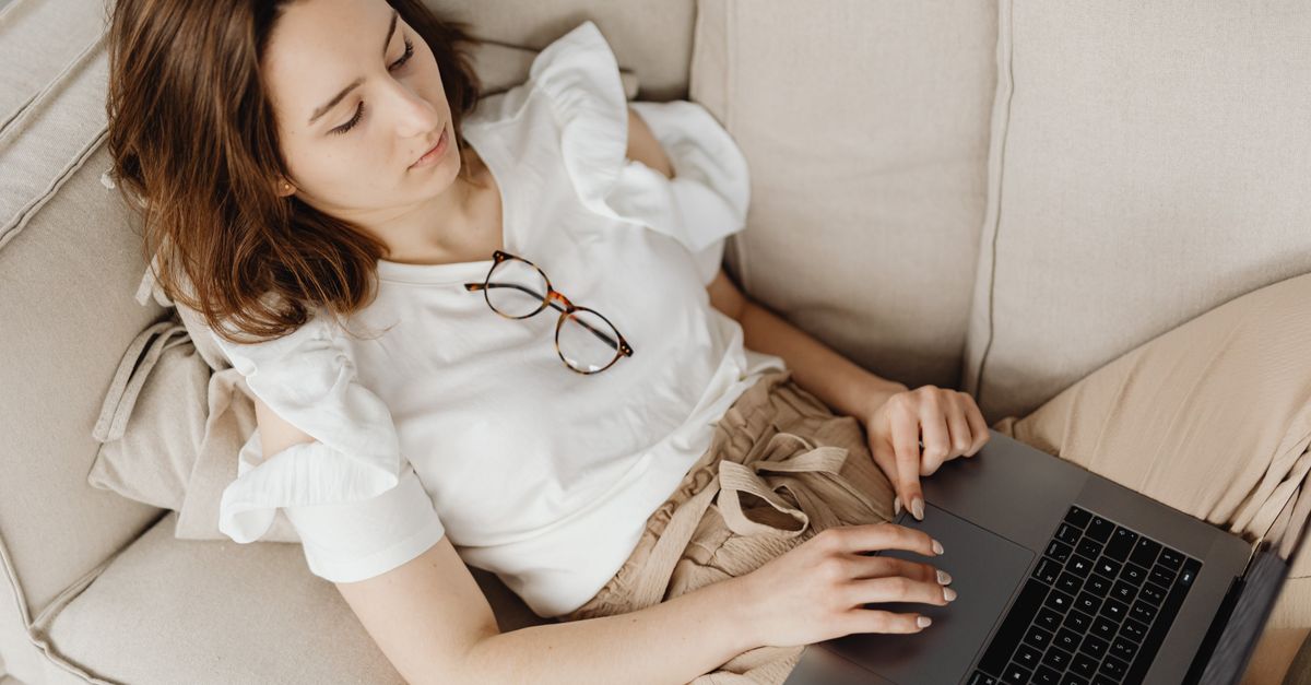 Young woman lying on a couch using a laptop, embodying remote work lifestyle.