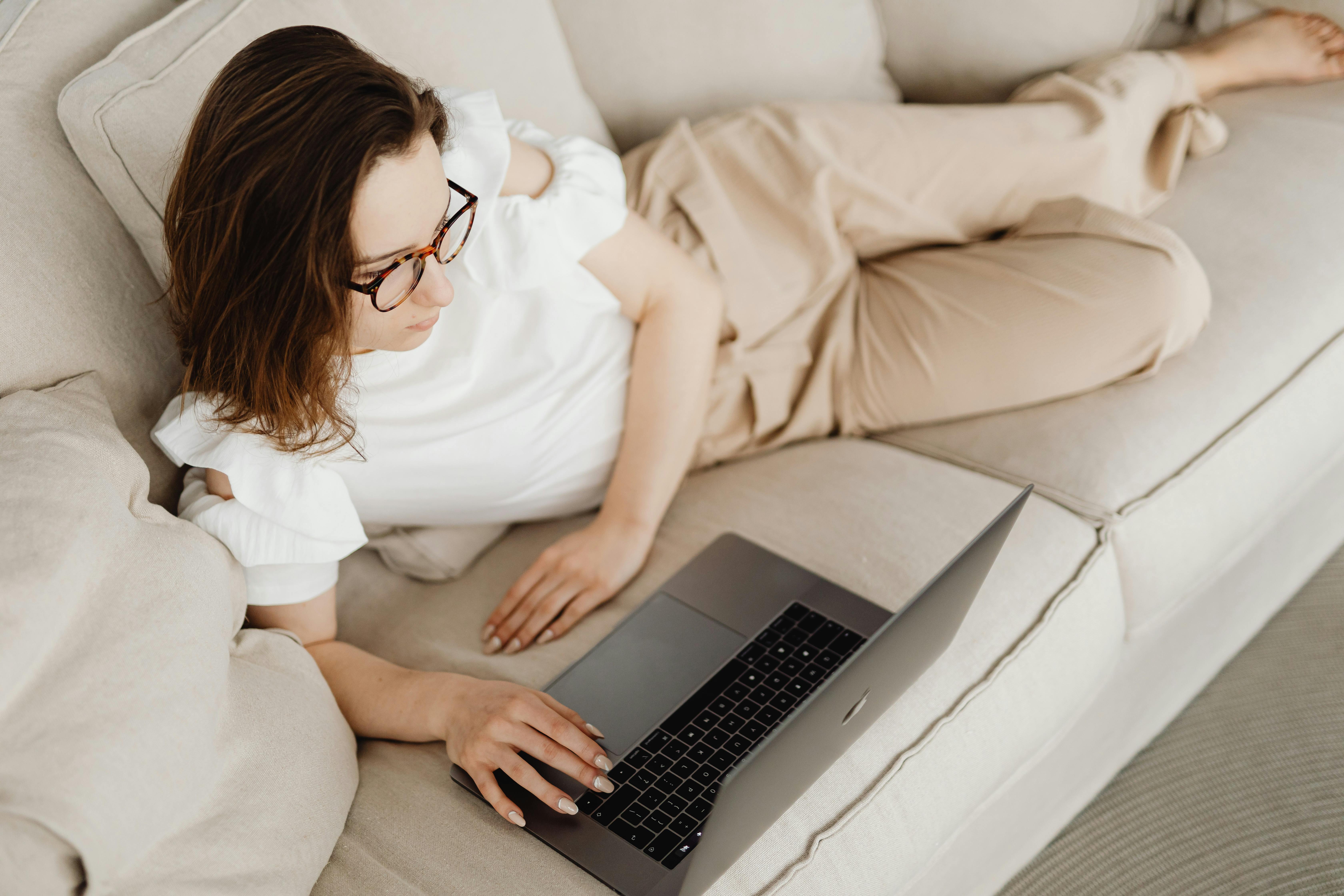 a woman lying on the couch looking at a laptop