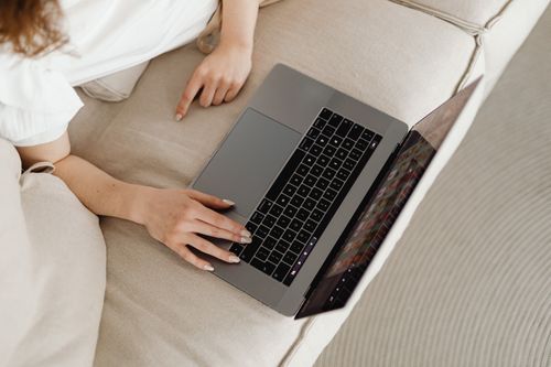 Free Close-up of a person working from home on a laptop, comfortable on a beige couch. Stock Photo