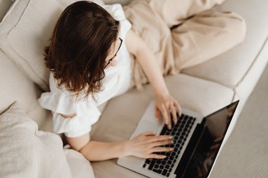 Adult woman typing on a laptop while relaxing on a couch, embracing remote work lifestyle.