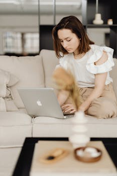 Young woman sitting on a couch working on her laptop in a cozy home setting.