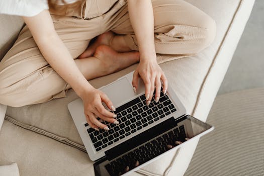 Overhead shot of a woman using a laptop while sitting cross-legged on a sofa.