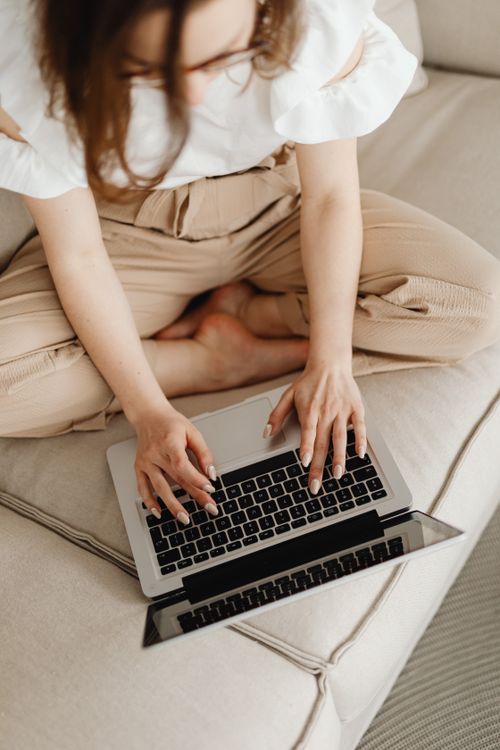 Free Top view of a woman sitting cross-legged on a couch typing on a laptop. Stock Photo