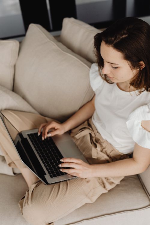 Free Caucasian woman working on a laptop while seated on a sofa indoors. Stock Photo