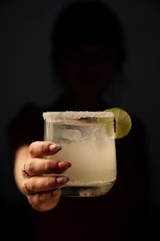 Close-up of a hand holding a margarita with lime, highlighting freshness.