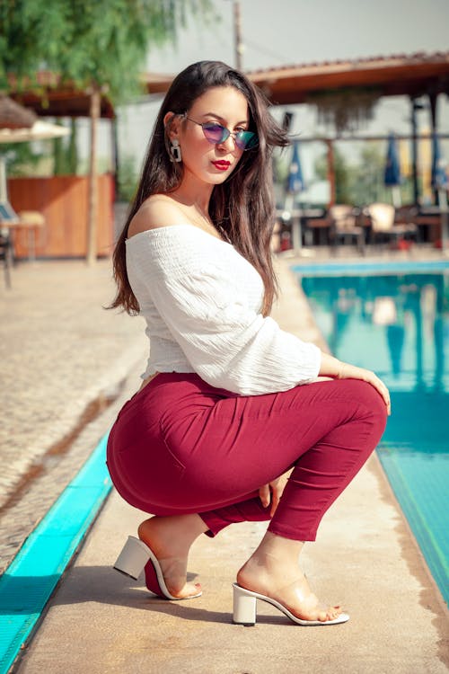 Free Photo of a Woman in Red Pants Crouching on the Poolside Stock Photo