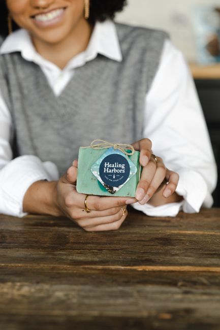 A smiling woman holds a handmade herbal soap, showcasing sustainable personal care products.
