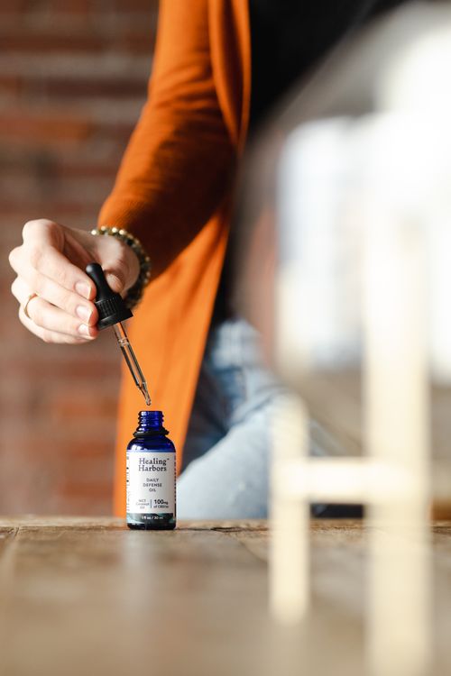 Free Close-up of a hand holding a dropper with CBD oil bottle on a table. Stock Photo