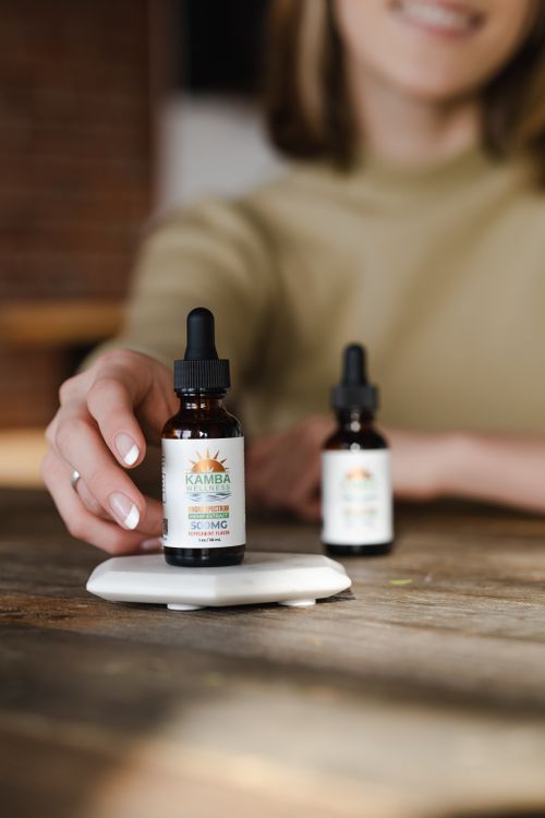 Free Close-up of a hand reaching for CBD oil bottle with dropper on wooden table. Stock Photo