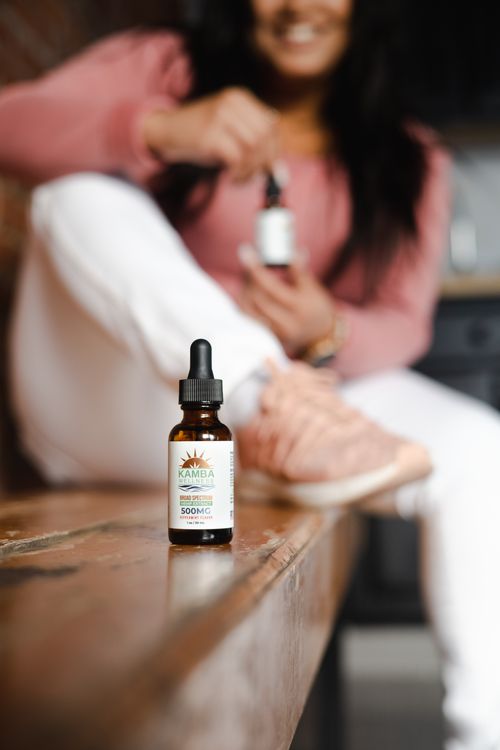 Free Focus on a Kamba wellness dropper bottle with a smiling woman holding another bottle in the background. Stock Photo