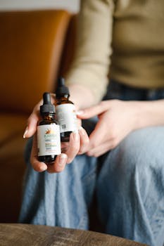 Close-up of hands holding Kamba Wellness dropper bottles indoors.