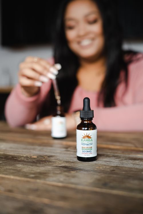 Free Herbal tincture bottle with focus, held by a smiling woman, indoors on wooden table. Stock Photo