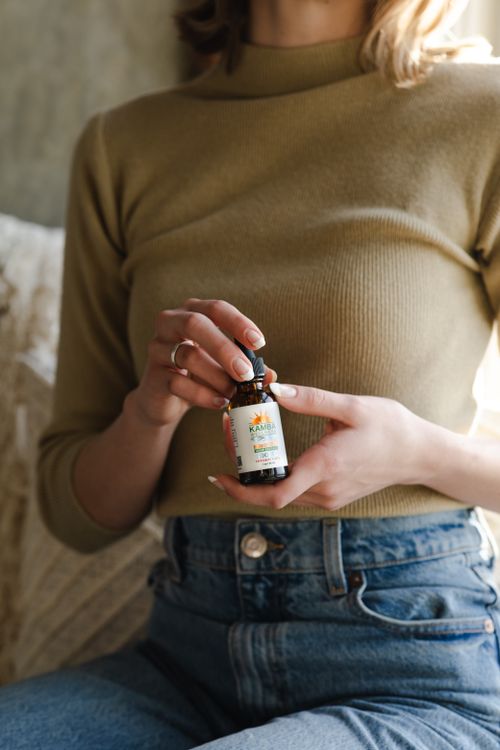 Free A woman wearing a sweater and jeans holding a CBD oil bottle indoors. Stock Photo