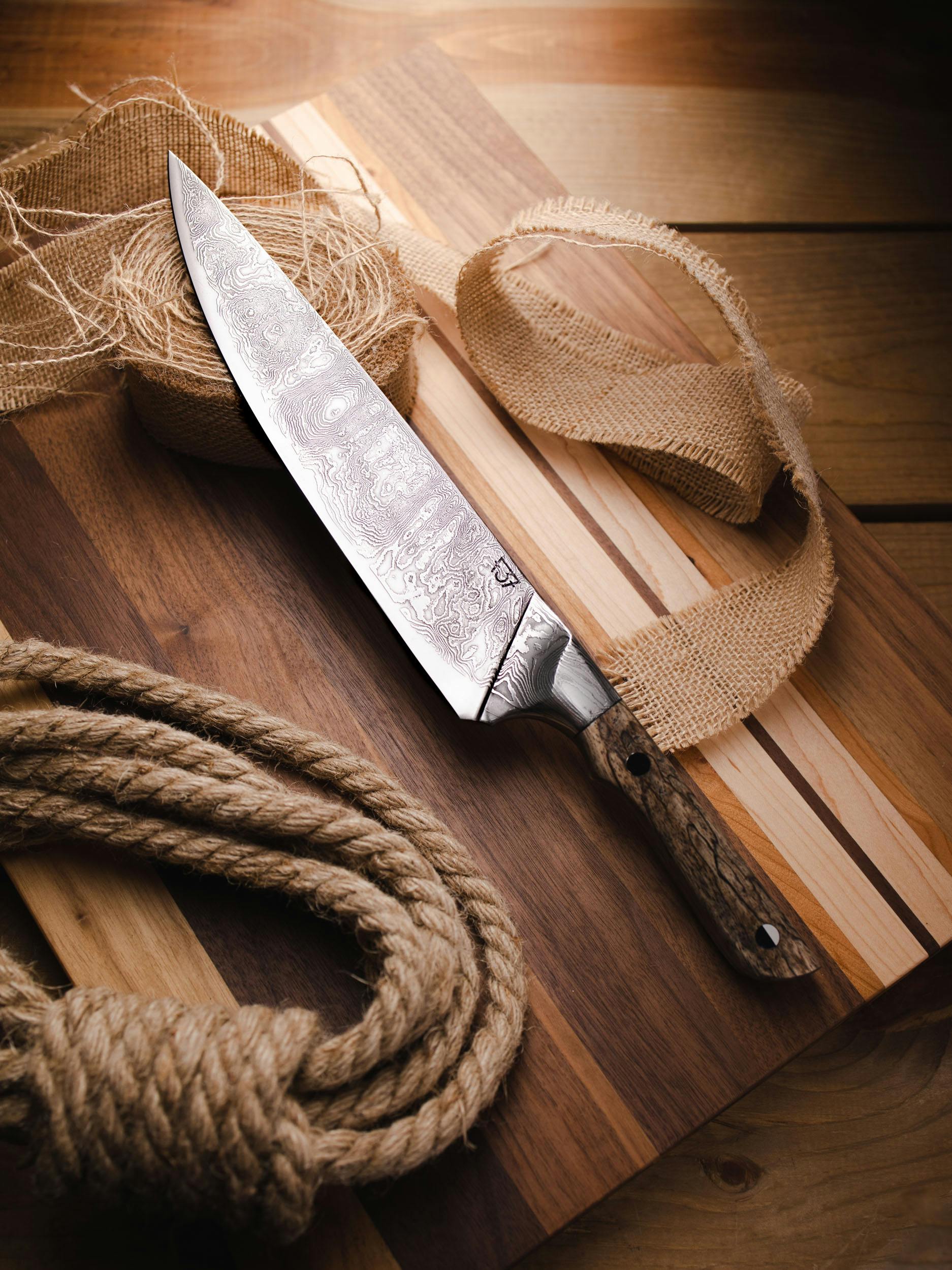 A beautifully crafted chef's knife placed on a wooden board with rustic ropes. Perfect for culinary use.