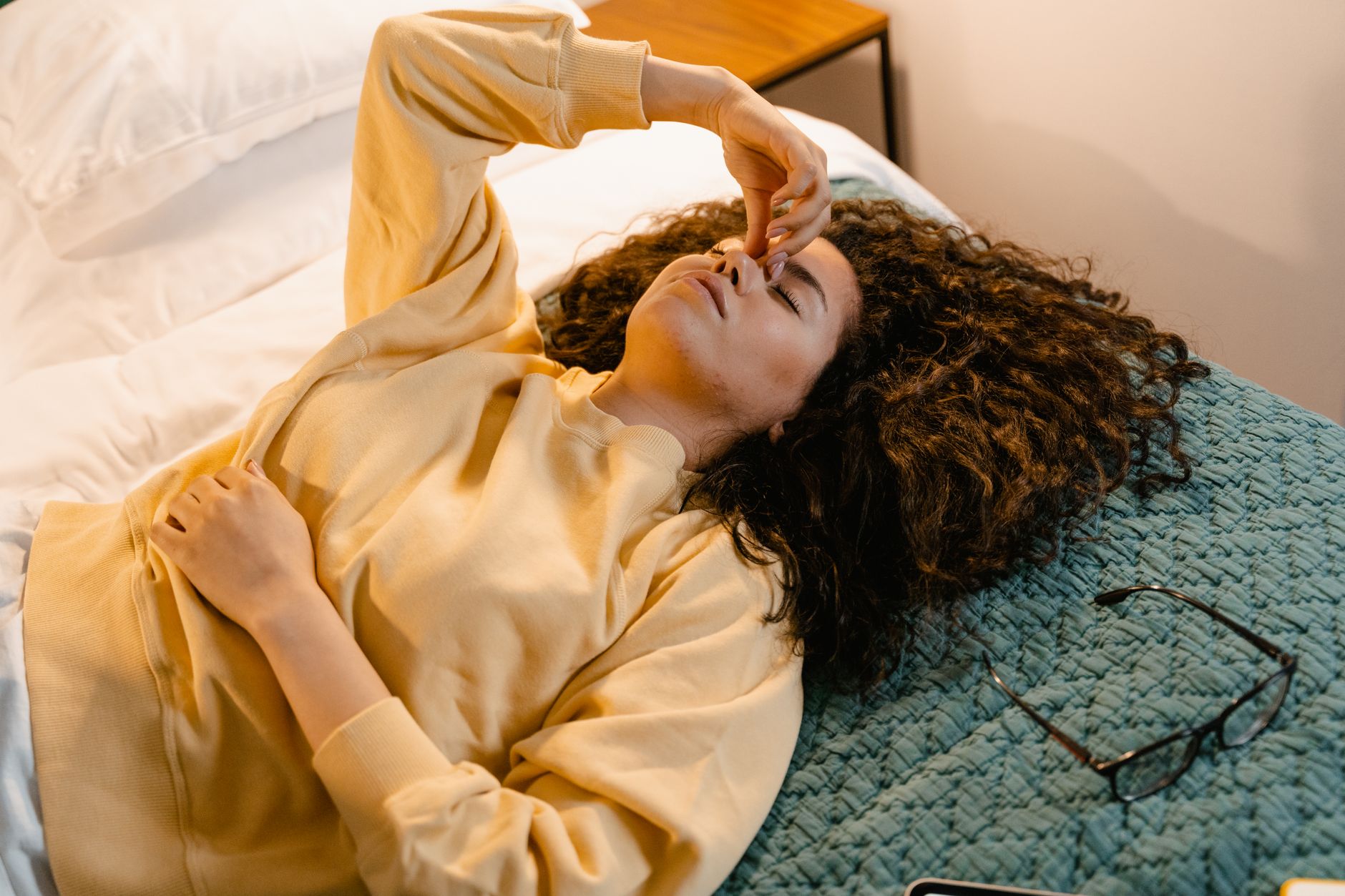 Ivermectin for long covid fatigue — A woman in a sweatshirt rests on a bed, showing a moment of relaxation and comfort indoors.