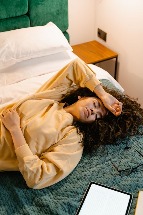 Free Young woman in yellow sweater resting on bed with a digital tablet nearby, capturing a calm indoor moment. Stock Photo