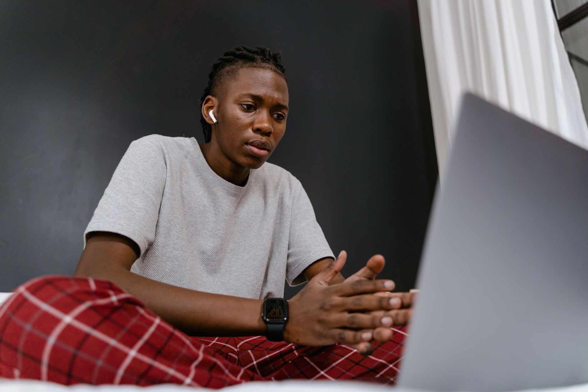 A young man in casual attire participates in a video call from home, sitting comfortably with a laptop.