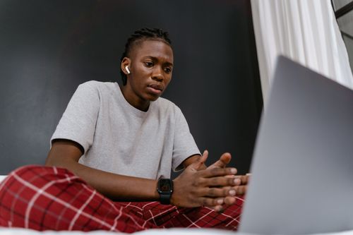 Free A young man in casual attire participates in a video call from home, sitting comfortably with a laptop. Stock Photo