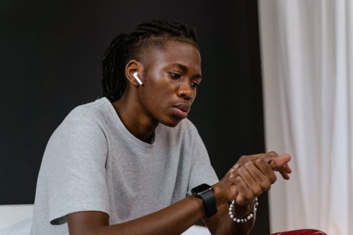 Free A young man wearing earbuds sits indoors, looking thoughtful and focused. Stock Photo