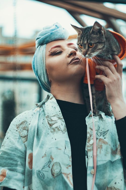 Free A woman with a headscarf holds a tabby cat while smiling outdoors. Warm and candid moment. Stock Photo
