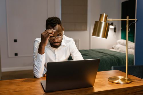 Free African American man working intently on a laptop in a bedroom setting, symbolizing remote work lifestyle. Stock Photo