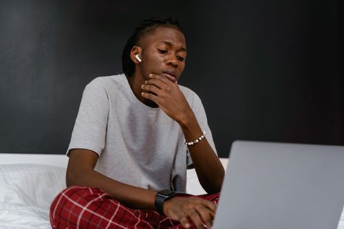 Free Focused young man with AirPods using a laptop while enjoying music indoors. Stock Photo