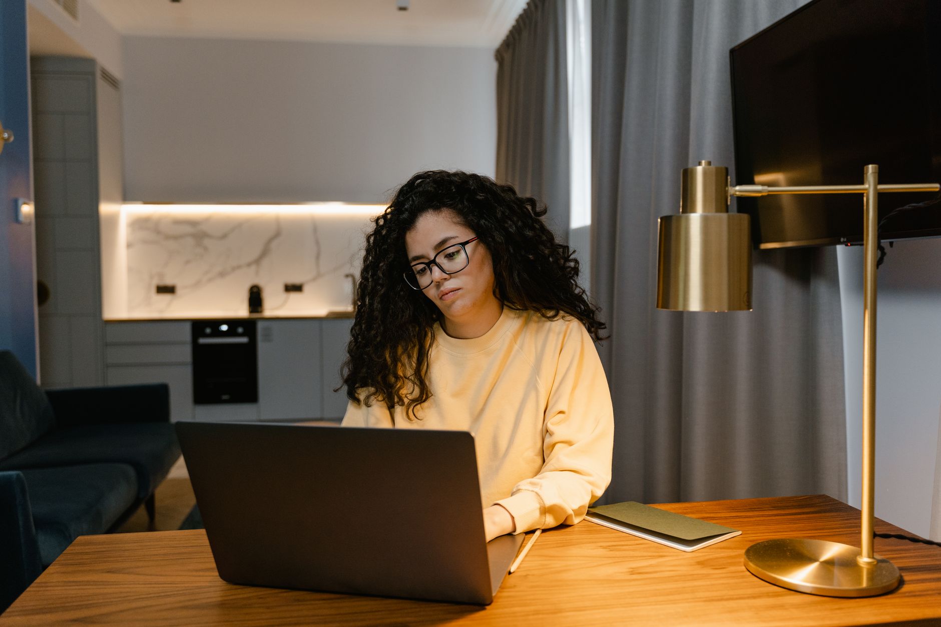 Woman in a yellow sweatshirt using a laptop at home, focusing on remote work in a cozy, modern interior.