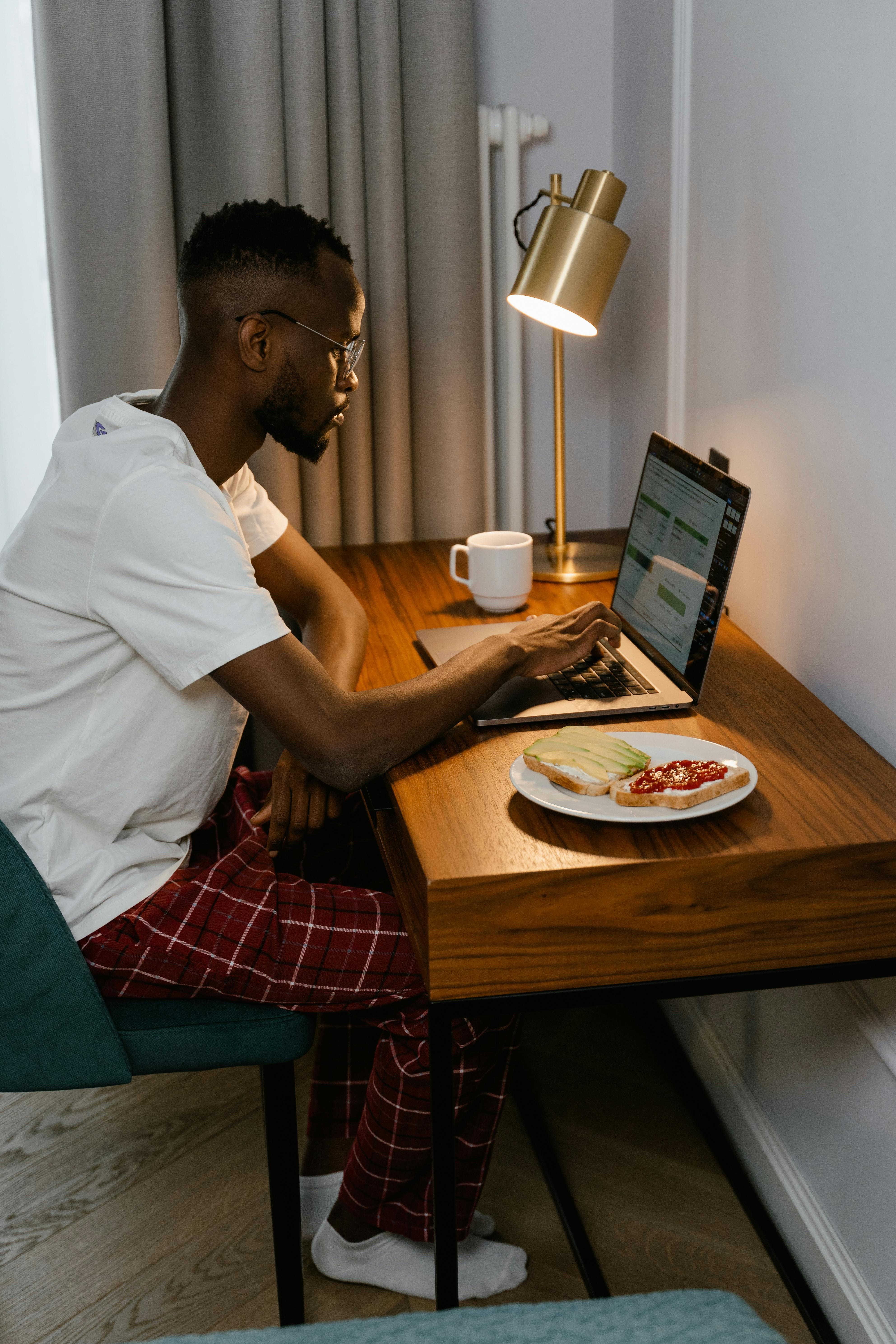 Casual morning work setup with laptop, coffee, and breakfast on a wooden desk.